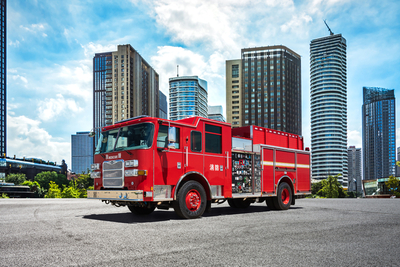 A red ultra high rise pumper fire truck is parked with large skyscrapers in the background.