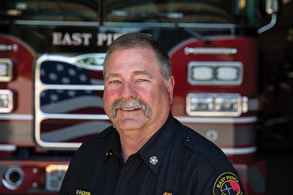 East Pierce Fire Chief smiling in front of Pierce aerial tiller ladder fire truck