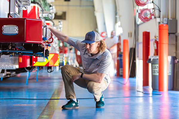 A man kneeling by the front bumper of a Fire Truck to inspect it on the Blue Floor at the Pierce Manufacturing facility.