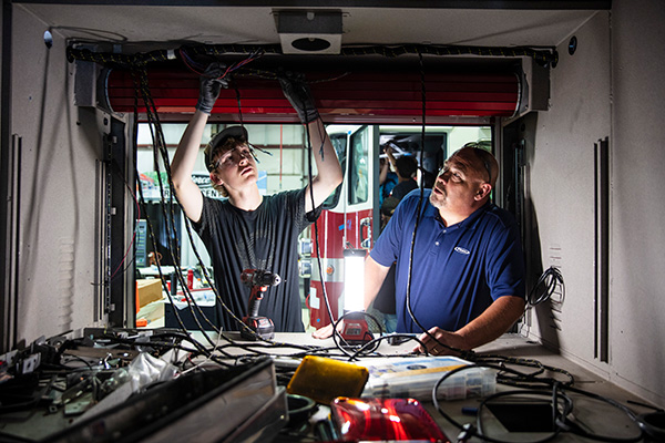 A Pierce employee training a man to wire a Fire Truck inside of the Pierce Manufacturing Facility.