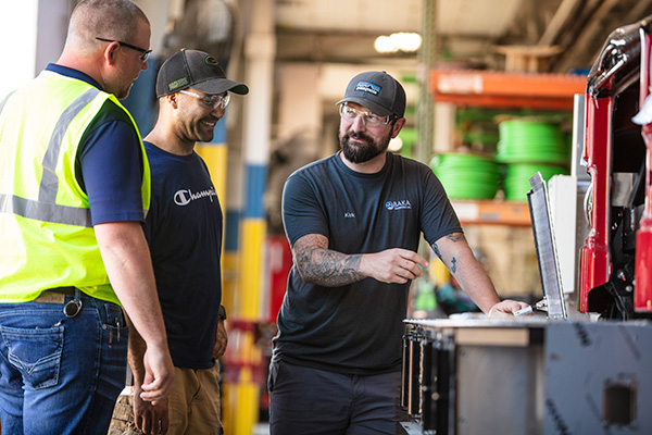 Three Pierce Manufacturing employees standing near a table talking in the Fire Truck manufacturing facility.