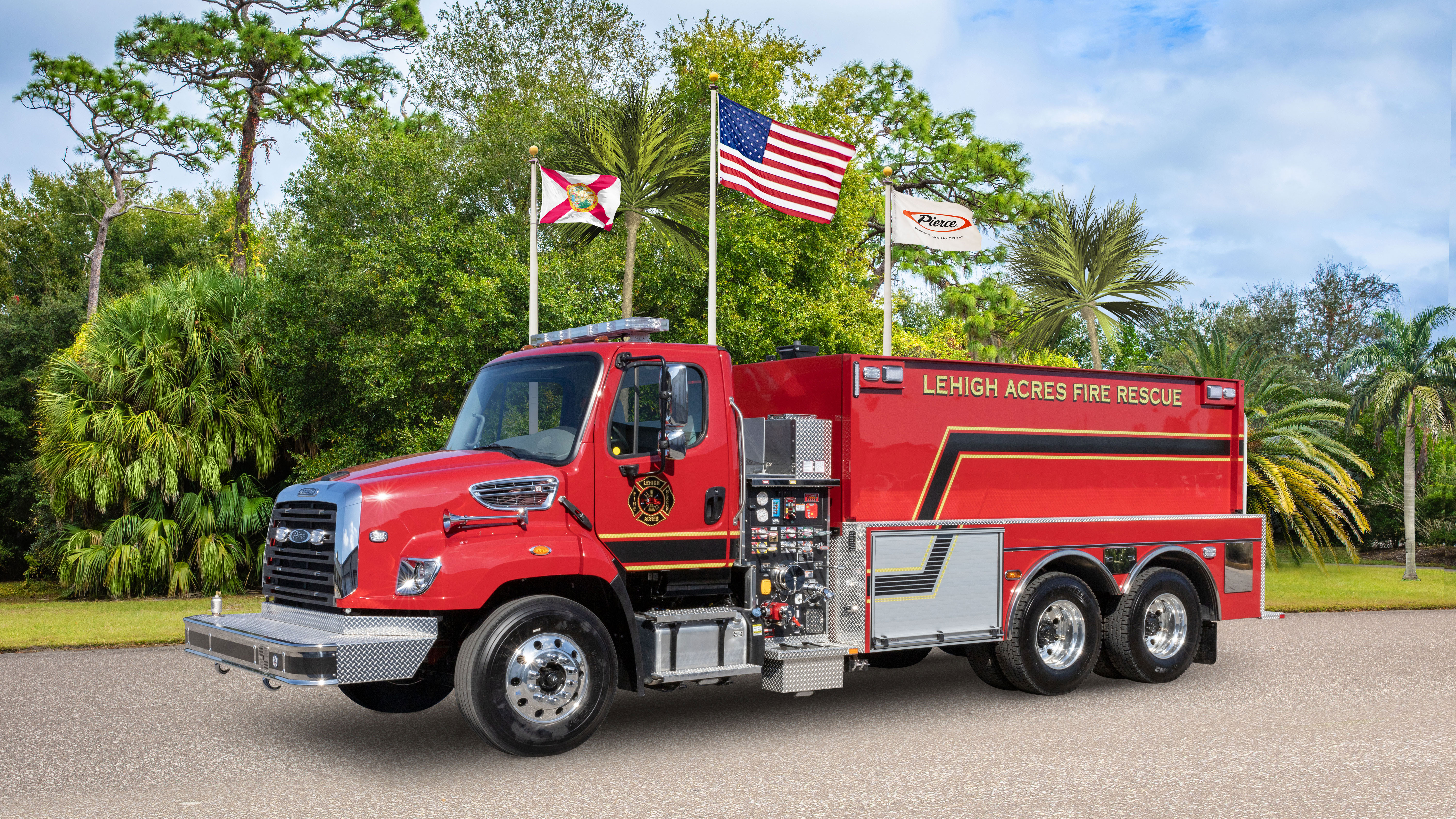 Pierce BX™ Tanker Fire Truck parked outside near trees and three flags on a sunny day. 