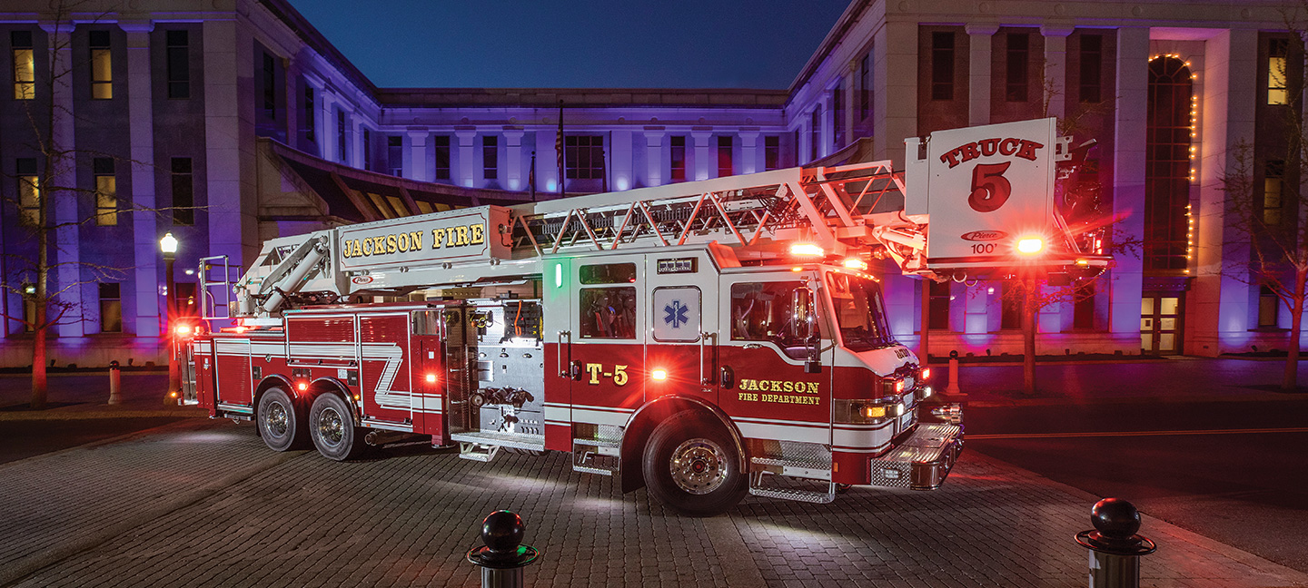 Pierce aerial fire truck with emergency lights on in front of Jackson, Tennessee city building
